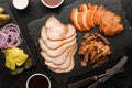Sliced Ã¢â¬â¹Ã¢â¬â¹smoked turkey fillet, smoked puilled pork and pickled vegetables set on a slate board, top view.